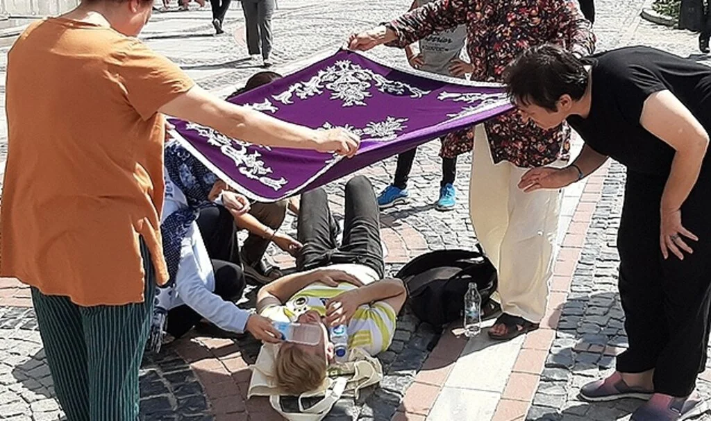 Kadınlar yerde yatan yaralıyı örtü ile güneşten korudu